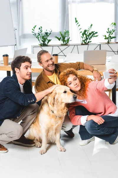 Trois amis souriants prenant selfie avec golden retriever mignon — Photo de stock