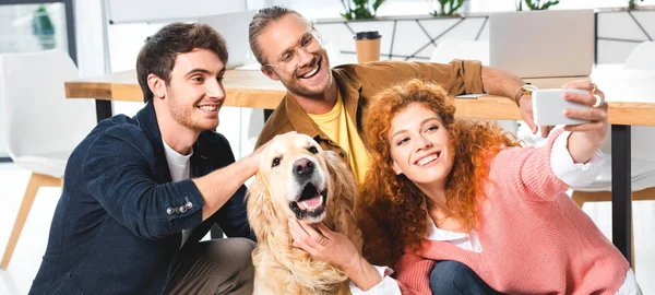 Panoramic shot of three smiling friends taking selfie with cute golden retriever — Stock Photo