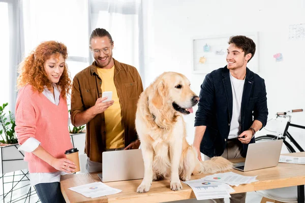 Three friends smiling and cute golden retriever sitting on table — Stock Photo