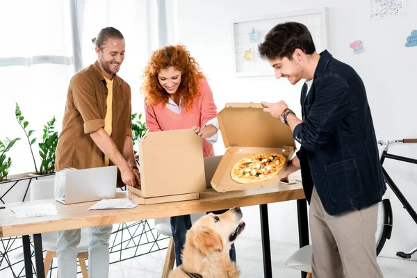 Tres demonios sonrientes sosteniendo cajas con pizza en la oficina - foto de stock