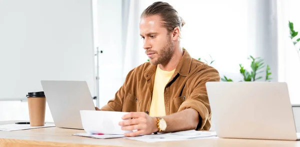 Panoramic shot of handsome man doing paperwork and looking at laptop — Stock Photo