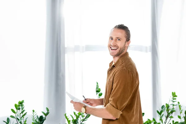 Uomo bello e sorridente in camicia che fa scartoffie in ufficio — Foto stock