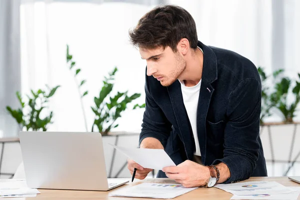 Bell'uomo che fa scartoffie e guarda il portatile in ufficio — Foto stock