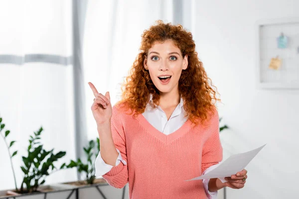 Attractive and shocked businesswoman showing idea sign and holding paper — Stock Photo