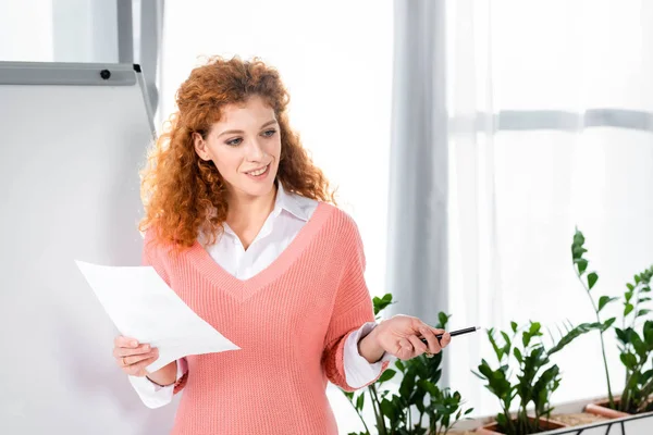 Femme d'affaires attrayante et souriante en pull rose tenant papier et stylo — Photo de stock