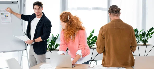 Panoramaaufnahme von Geschäftsleuten, die einen Freund anschauen, der Papier mit Diagrammen und Grafiken zeigt — Stockfoto