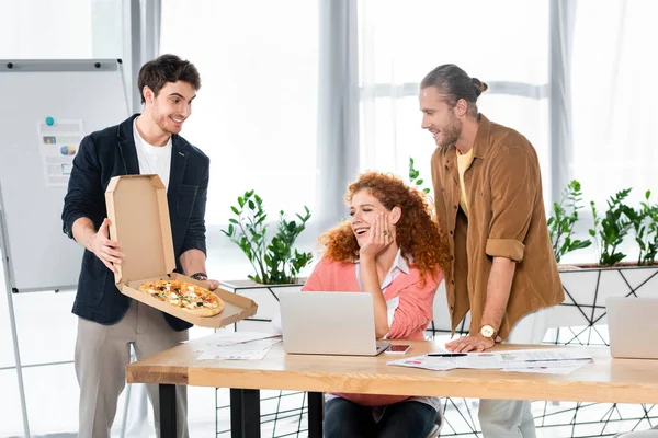 Empresarios sonrientes mirando a un amigo con caja de pizza - foto de stock