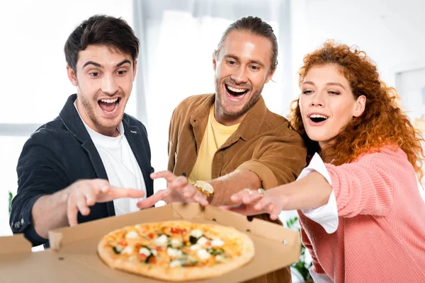 Foco seletivo de três amigos sorridentes tirando pizza da caixa — Fotografia de Stock