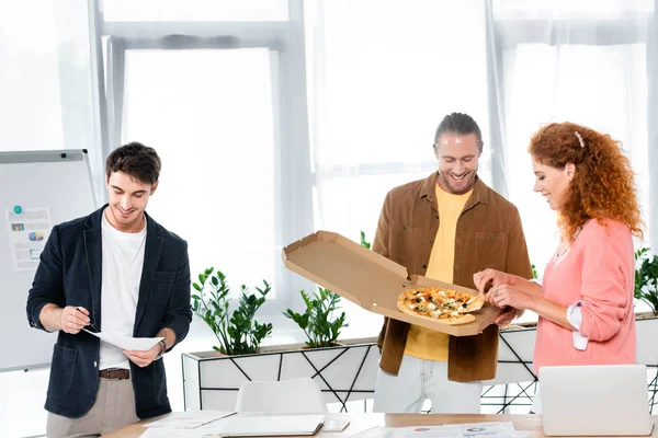 Amis souriants prendre la pizza de la boîte et faire de la paperasse — Photo de stock