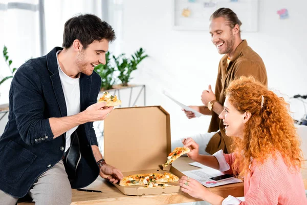 Tre amici sorridenti che prendono la pizza dalla scatola in ufficio — Foto stock