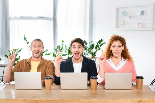 Drei schockierte Freunde sitzen am Tisch und zeigen Ideenschilder — Stockfoto