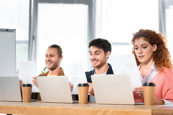 Três amigos sorridentes sentados à mesa e fazendo papelada — Fotografia de Stock