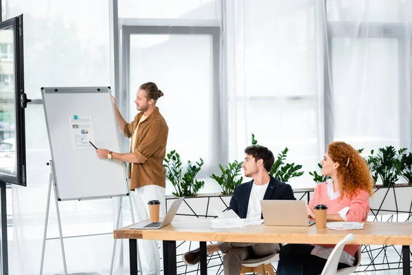 Handsome businessman pointing at paper with graphs and charts to his friends — Stock Photo