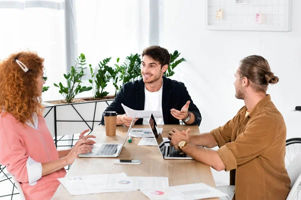Three smiling friends holding paper and talking in office — Stock Photo