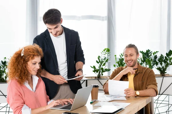 Three friends using laptop, holding digital tablet and doing paperwork — Stock Photo