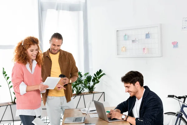 Друзья смотрят на цифровой планшет и человека с ноутбуком в офисе — стоковое фото