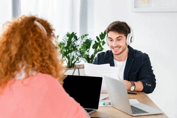 Selective focus of smiling and handsome man in headphones using laptop — Stock Photo
