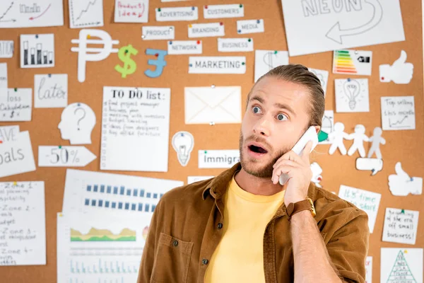 Guapo y sorprendido hombre de negocios hablando en el teléfono inteligente en la oficina - foto de stock