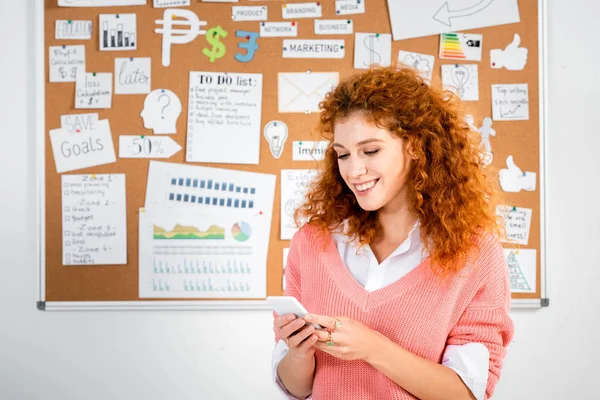 Attraktive Geschäftsfrau im rosa Pullover, die lächelt und ihr Smartphone in der Hand hält — Stockfoto