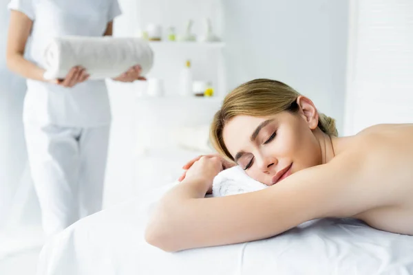 Приваблива жінка з закритими очима лежить на масажному килимку в спа-центрі — стокове фото