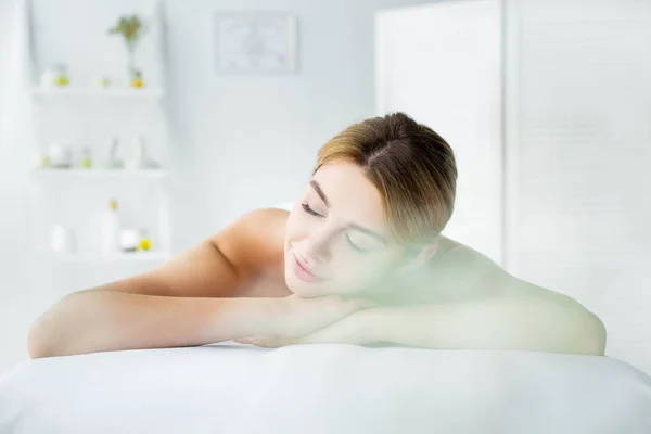 Atractiva mujer con los ojos cerrados acostada en la alfombra de masaje en el spa - foto de stock