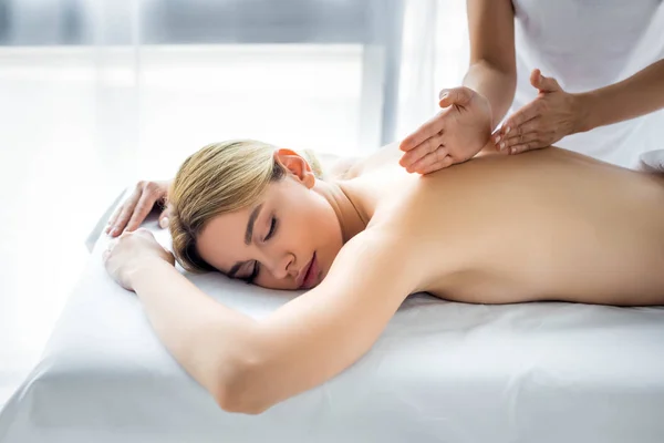Обрезанный вид массажера, делающего массаж спины привлекательной женщине в спа — стоковое фото