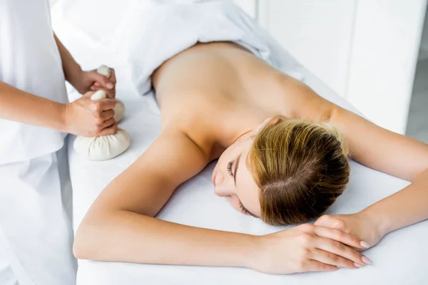 Vista cortada de massagista fazendo massagem nas costas com bolas de ervas para a mulher no spa — Fotografia de Stock
