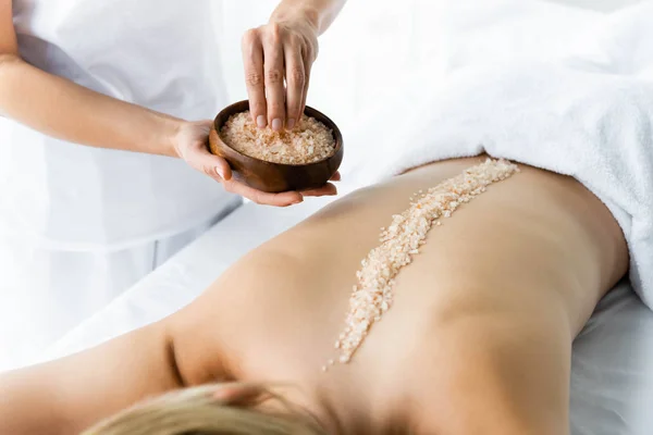 Cropped view of masseur applying sea salt on back of woman — Stock Photo