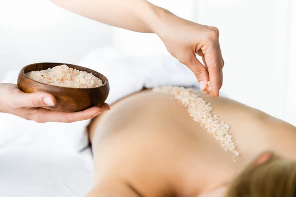 Cropped view of masseur applying sea salt on back of woman — Stock Photo