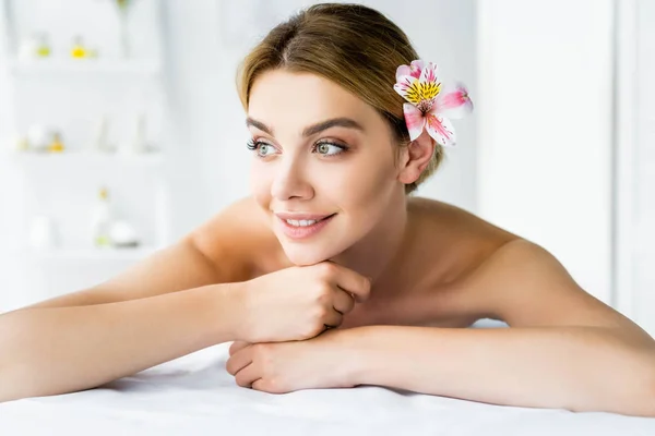 Atractiva y sonriente mujer con flor acostada en alfombra de masaje - foto de stock