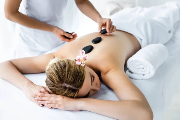 Vista ritagliata di massaggiatore facendo massaggio con pietre calde alla donna in spa — Foto stock