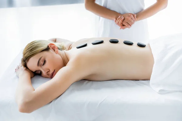 Cropped view of masseur doing hot stone massage to woman in spa — Stock Photo