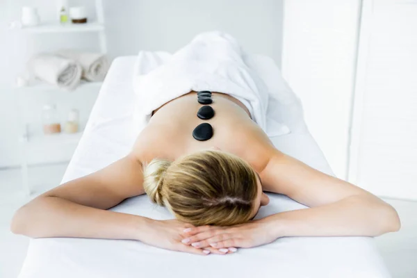 Mujer con piedras calientes en la espalda acostado en alfombra de masaje — Stock Photo
