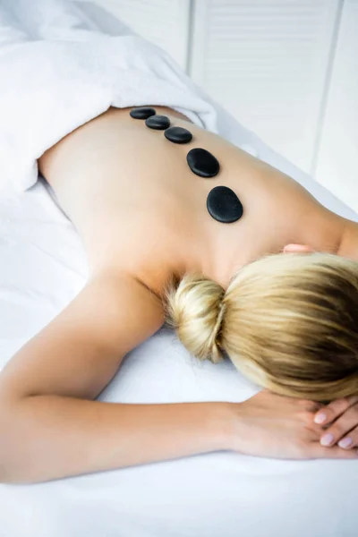 Donna con pietre calde sul retro sdraiato su tappetino da massaggio — Foto stock