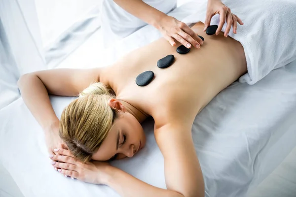 Обрезанный вид массажера, делающего массаж горячими камнями женщине в спа — стоковое фото