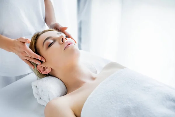 Recortado vista de masajista haciendo masaje facial a atractiva mujer - foto de stock