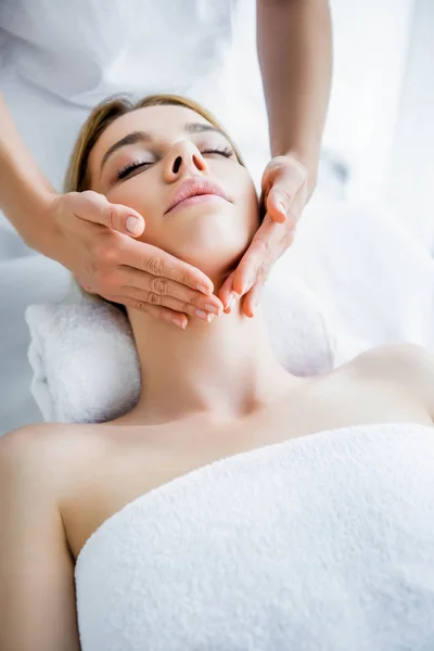 Recortado vista de masajista haciendo masaje facial a atractiva mujer - foto de stock