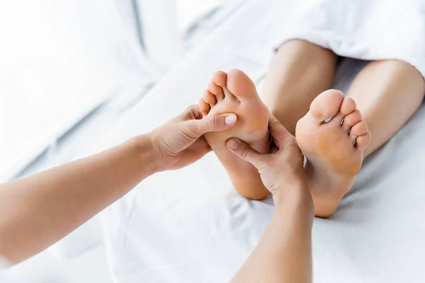 Обрезанный вид массажера, делающего массаж ног женщине в спа — стоковое фото