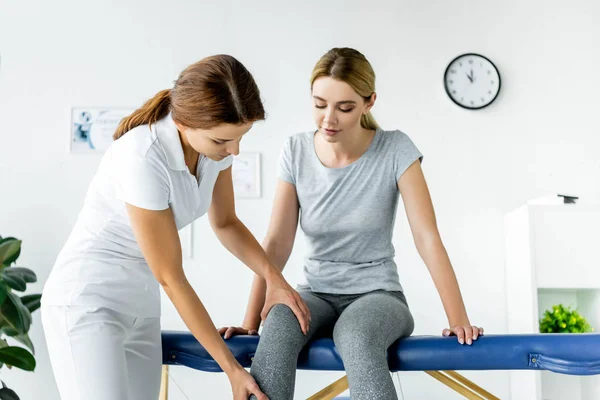 Chiropraktiker berührt Bein einer attraktiven Patientin im grauen T-Shirt — Stockfoto