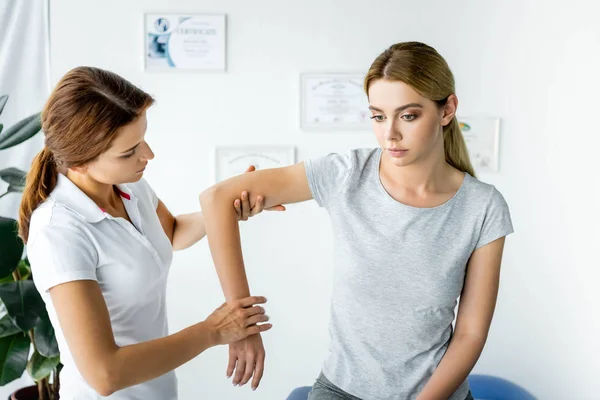 Хиропрактик трогает руку привлекательного пациента в серой футболке — стоковое фото