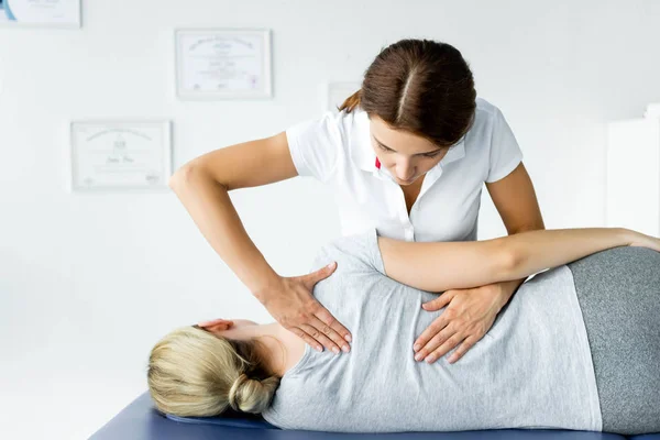 Attractive chiropractor touching hand of patient in grey t-shirt — Stock Photo