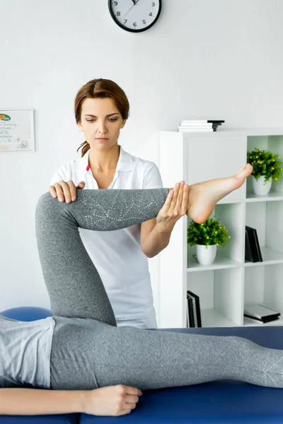 Vista recortada del quiropráctico tocando la pierna del paciente en leggins grises - foto de stock