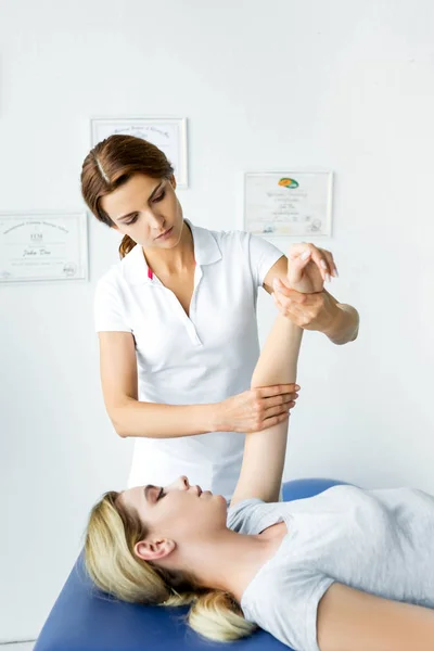 Quiropráctico tocando mano de atractiva paciente en camiseta gris - foto de stock