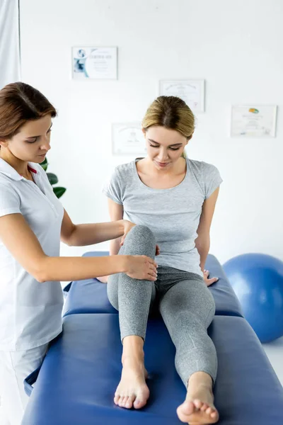 Quiropráctico tocando pierna de atractiva paciente en camiseta gris - foto de stock