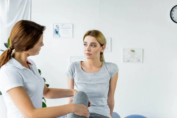 Chiropraktiker berührt Bein einer attraktiven Patientin im grauen T-Shirt — Stockfoto