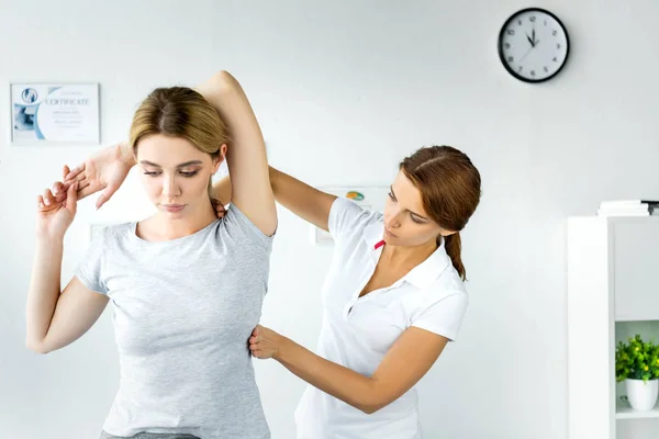 Quiropráctico tocando mano de atractiva paciente en camiseta gris - foto de stock