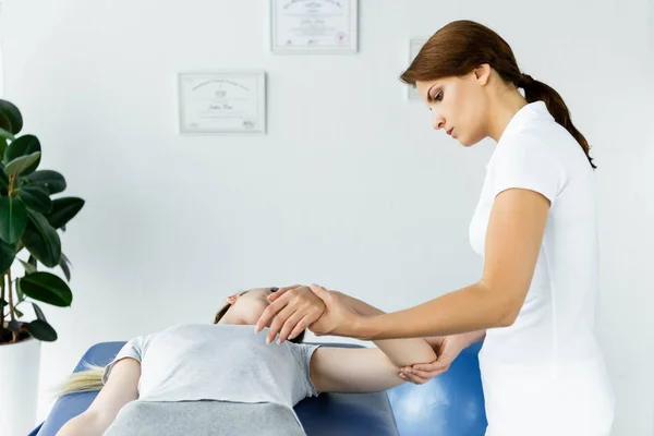 Quiropráctico tocando la mano del paciente en camiseta gris en clínica - foto de stock