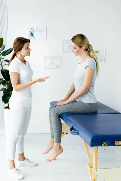 Chiropractor talking with attractive patient in t-shirt in clinic — Stock Photo