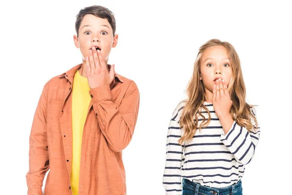 Visão frontal de crianças chocadas cobrindo bocas com mãos isoladas em branco — Fotografia de Stock