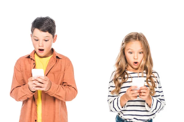 Vista frontal de niños conmocionados utilizando teléfonos inteligentes aislados en blanco - foto de stock